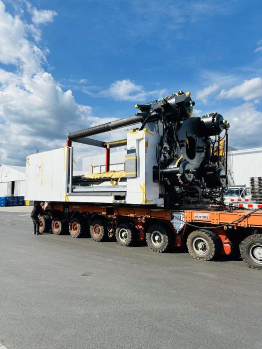 Załadunek wtryskarki z użyciem specjalistycznej platformy transportowej na terenie zakładu przemysłowego. 