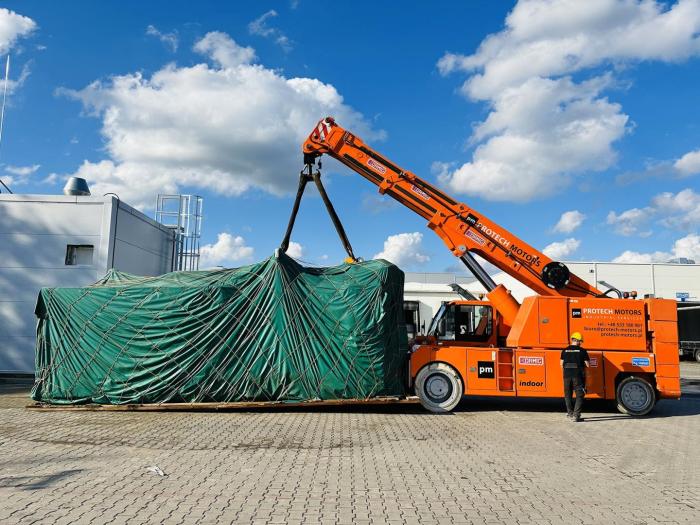 Transport wtryskarki owiniętej plandeką przy użyciu dźwigu samojezdnego na terenie zakładu. 