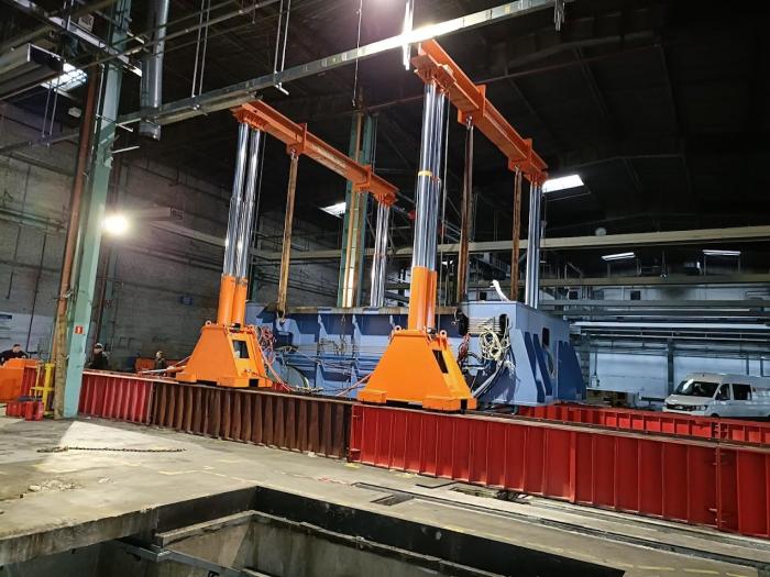 Uniesiony element prasy AIDA stabilizowany na podporach podczas demontażu w hali. 