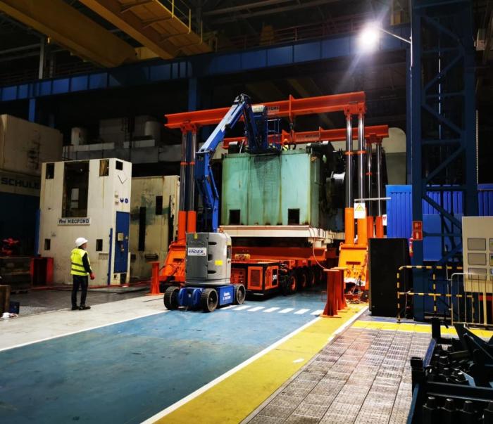 Transport prasy mechanicznej na specjalistycznej platformie w hali produkcyjnej. 