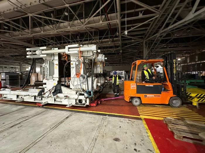 Wózek widłowy wspierający relokację maszyny przemysłowej na terenie hali produkcyjnej. 